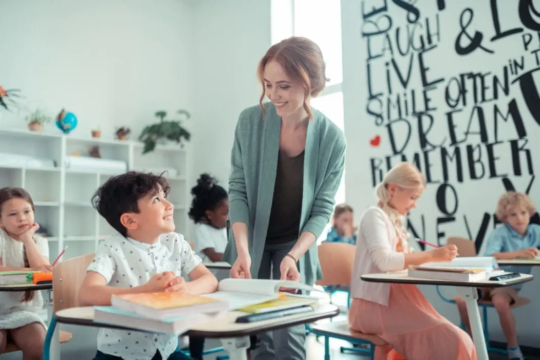Teacher and her student in a classroom smiling at each other.