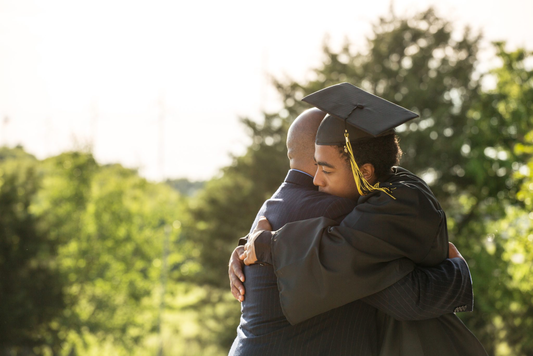 College graduate in cap and gown hugging his father.